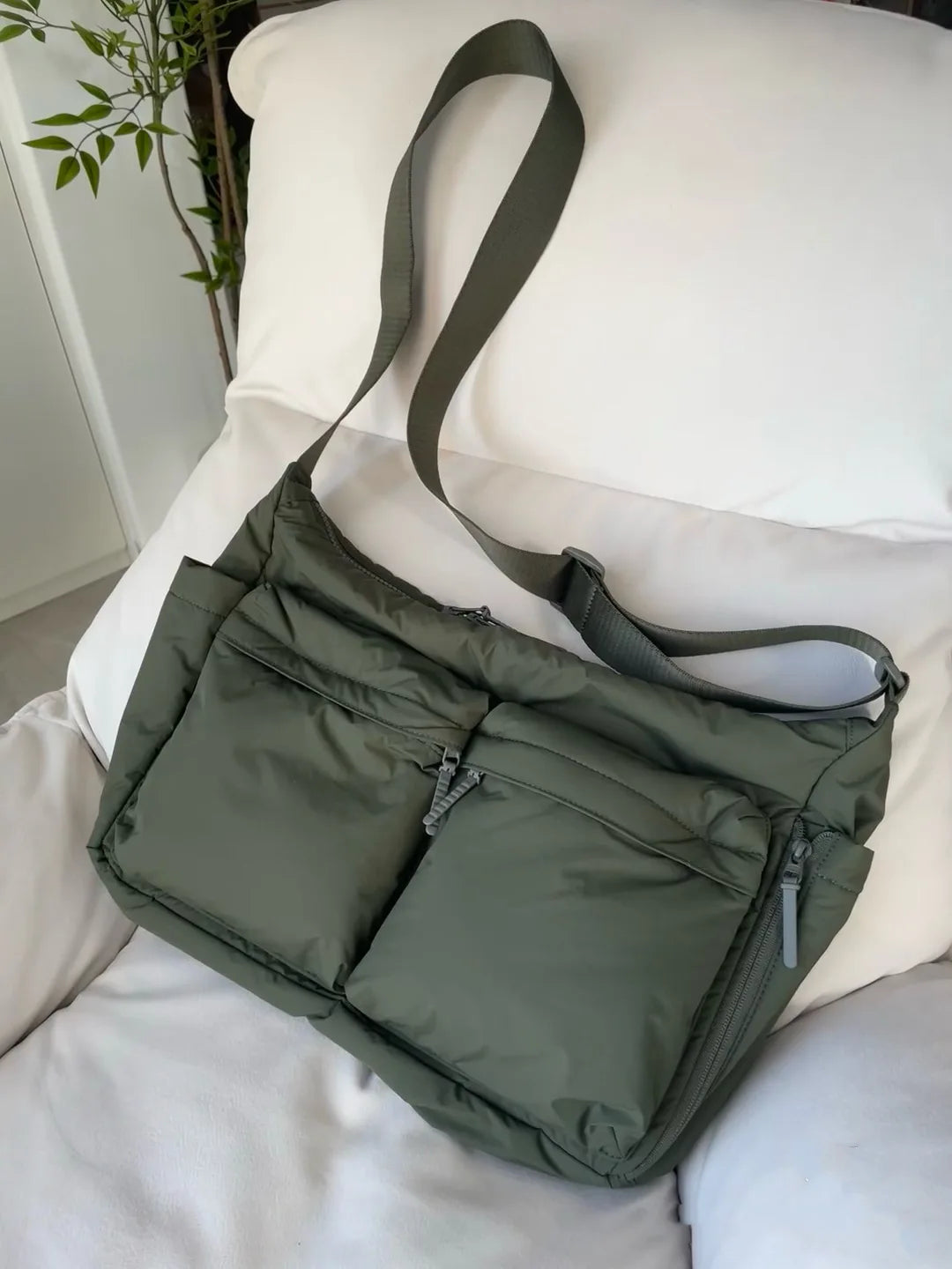 Green shoulder bag on a white surface with a plant in the background